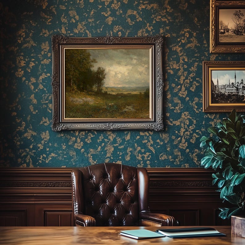 A victorian office interior, featuring an antique oil painting on a wall with blue and gold wallpaper. The painting is a moody landscape that is frame in a vintage ornate frame. The artwork is hung above a wooden desk with a tufted leather chair.