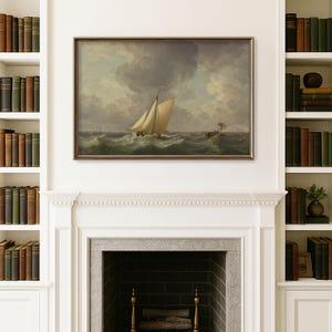 May include: A framed painting of a sailboat at sea, with a stormy sky overhead. The artwork is displayed above a fireplace, flanked by bookshelves filled with antique books. The painting's frame is a dark, warm color.