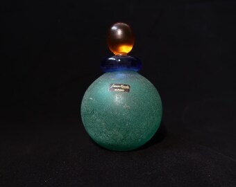May include: A green glass bottle with a frosted finish and a blue and orange stopper. The bottle has a label that reads "Antica Murrina Murano".