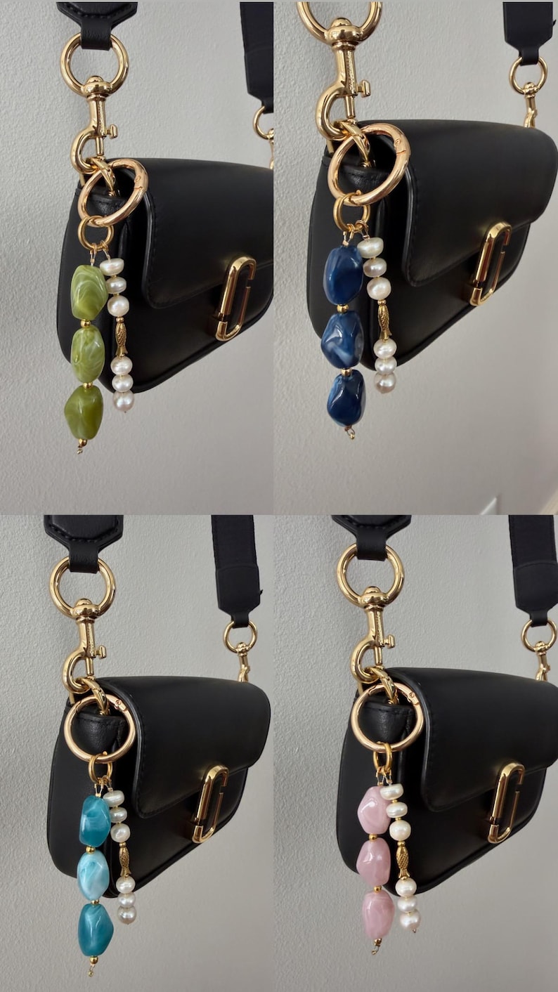 Puede incluir: Un bolso bandolera de cuero negro con herrajes dorados. Cada bolso presenta un charm &uacute;nico: cuentas de piedras preciosas verdes, azules, turquesas o rosas, acentuadas con perlas, colgando de un anillo dorado.