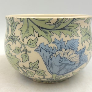 May include: A white ceramic bowl with a floral design. The bowl features blue and green flowers and leaves on a white background.