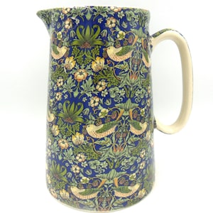 May include: A blue ceramic jug with a floral and bird pattern. The jug has a white handle and a wide mouth.