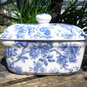 Peut inclure: Un plat en céramique blanc avec un motif floral bleu, de forme rectangulaire avec un couvercle et un petit bouton. Le design est de style bleu et blanc classique, adapté pour servir ou conserver des aliments.