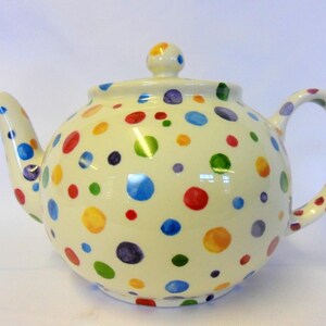 May include: Cream-coloured ceramic teapot with a lid and handle, decorated with a pattern of colourful polka dots in red, blue, yellow, green, and purple. The teapot has a spout for pouring and a knob on the lid.