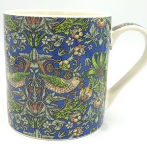 May include: A blue ceramic mug with a floral pattern featuring birds and berries. The mug has a white handle.