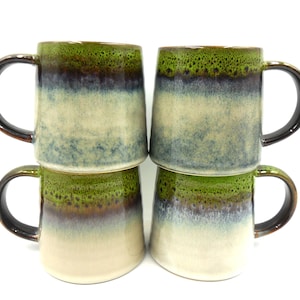 May include: Set of four ceramic mugs with a green, brown, and white glaze. The mugs have a speckled finish and a rounded shape.