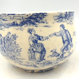 May include: A white ceramic bowl with a blue and white design. The design features a couple holding hands and a dog. The bowl is a vintage piece.