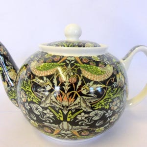 May include: A patterned ceramic teapot. The black body is decorated with a floral and bird design in green, yellow, and orange. The spout, handle, and lid are white. The teapot has a round body and a curved spout.