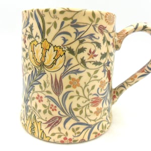 May include: A ceramic mug with a floral pattern in shades of yellow, red, blue, and green. The mug has a white background and a handle.