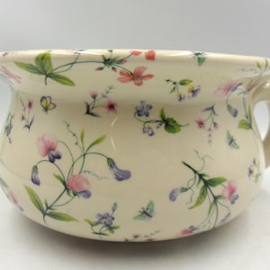 May include: A white ceramic bowl with a floral pattern. The bowl has a wide rim and a handle on one side. The floral pattern features pink, purple, and green flowers on a white background.