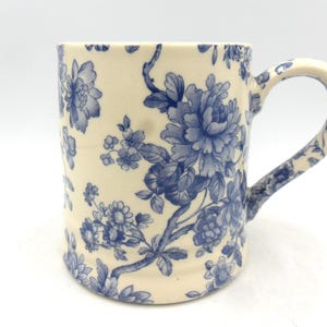 May include: A white ceramic mug with a blue floral pattern. The mug has a large handle and a wide base.