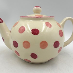 May include: Cream-coloured ceramic teapot with a lid and handle. The teapot is decorated with various sized pink and burgundy polka dots. The spout and lid rim are also accented with pink. A small knob sits atop the lid.