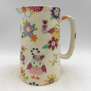 May include: A white ceramic jug with a colourful floral and owl pattern. The jug has a handle and a spout.