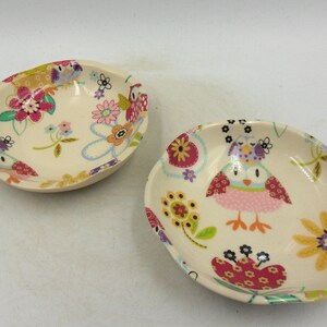 May include: Two white ceramic bowls with a floral and owl design. The bowls have a cream background with pink, yellow, blue, and green flowers and owls.