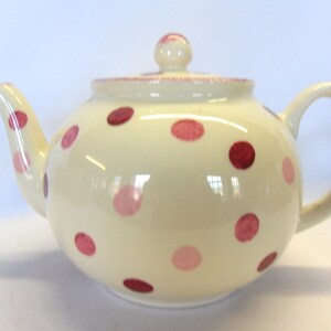 May include: A white teapot with pink and red polka dots. The teapot has a round body and a curved spout.
