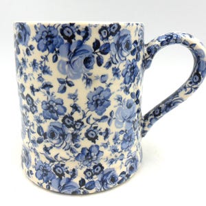 May include: A white ceramic mug with a blue floral pattern. The mug has a wide, rounded handle.