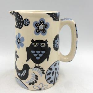 May include: A white ceramic jug with a blue and black owl, bird, and floral pattern.