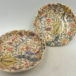 Peut inclure: Deux bols en céramique décoratifs avec un motif floral dans des tons de bleu, jaune, rouge et vert sur un fond crème.
