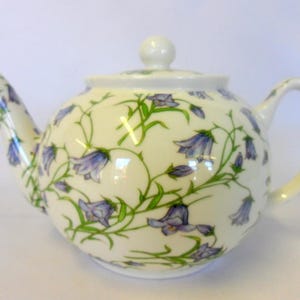 May include: A white porcelain teapot with a floral design featuring bluebell flowers and green leaves. The teapot has a lid and a handle.