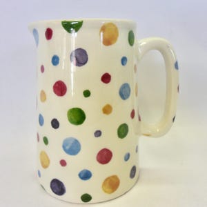Peut inclure: Un pichet en céramique blanche avec un motif de pois multicolores. Les pois sont dans des tons de rouge, vert, bleu, jaune et violet.