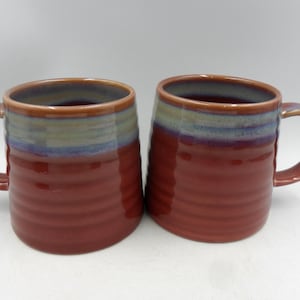 May include: Two red ceramic mugs with a blue and green glaze. The mugs have a textured, ribbed design.