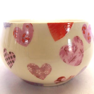 May include: A white ceramic bowl with a heart pattern. The hearts are pink, red, and purple with different designs.