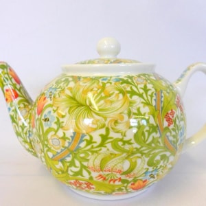 May include: A patterned ceramic teapot with a white lid and handle. The design features green, yellow, orange, and blue floral motifs. The teapot has a rounded shape and a curved spout.