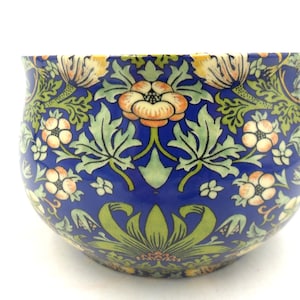 May include: A blue ceramic bowl with a floral pattern in shades of green, yellow, and orange. The bowl has a rounded shape and a wide rim.