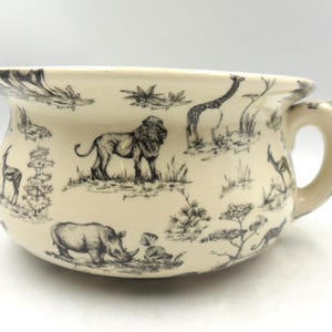 以下が含まれることがあります： 白地に黒と白の動物柄が描かれた白い陶器製の便器。ライオン、キリン、サイ、ヌーなど、アフリカの動物が描かれています。便器には側面に持ち手があります。