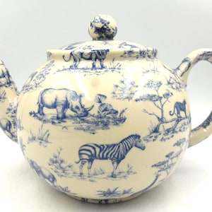 以下が含まれることがあります： シマウマ、サイ、ゾウなど、アフリカの動物が青と白のパターンで描かれた白いセラミック製のティーポット。ティーポットは丸いボディとノブ付きの蓋をしています。