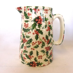 Peut inclure: Pichet en céramique crème, orné d'un motif de feuilles de houx vertes et de baies rouges. Le pichet est doté d'une anse et d'un bec verseur, parfait pour servir des boissons pendant les fêtes de fin d'année.