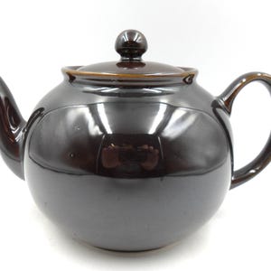 May include: A brown ceramic teapot with a rounded body and a lid with a knob. The teapot has a spout and a handle.