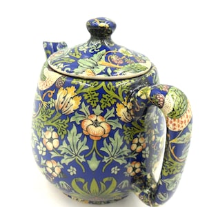 May include: A blue ceramic teapot with a floral design in orange, yellow, and green. The teapot features a lid and a curved handle. The pattern includes flowers, leaves, and birds, creating a decorative piece.