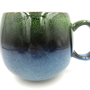 May include: A green and blue ceramic mug with a rounded body and a handle. The mug has a speckled glaze.