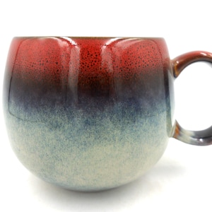 May include: A red, blue and white ombre ceramic mug with a rounded body and a handle.