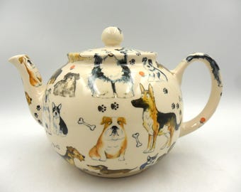 May include: Cream-colored ceramic teapot decorated with various dog breeds, paw prints, and bones. The teapot has a rounded body, a curved handle, and a spout. The lid is topped with a small, round knob.