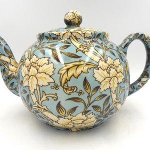 May include: A blue and white ceramic teapot with a floral pattern. The teapot has a round body and a curved spout. The handle is attached to the side of the teapot.