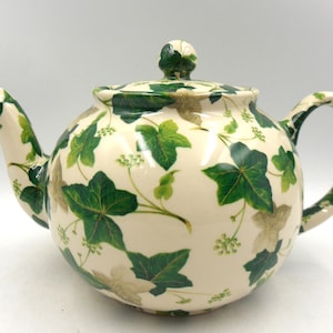 May include: A white teapot with a green ivy pattern. The teapot has a round body and a lid with a knob.