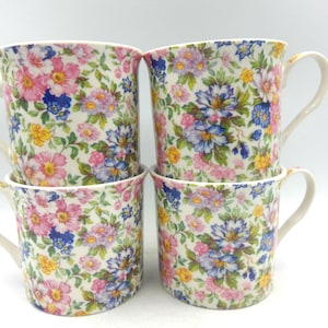 May include: Set of four white ceramic mugs with a floral pattern in shades of pink, blue and yellow. The mugs have a handle on the right side.