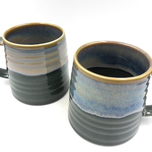 May include: Two ceramic mugs with a blue, brown and black glaze. The mugs have a textured, ribbed design on the bottom half.