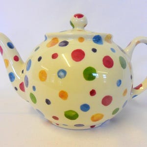 May include: A white ceramic teapot with a colourful polka dot pattern. The dots are in various shades of red, yellow, green, and blue.