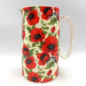 Peut inclure: Un pichet en céramique blanche avec un motif floral de coquelicots rouges. Le pichet a une anse et une large ouverture.