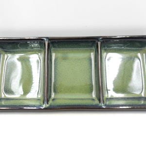 May include: A green ceramic serving dish with three divided sections. The dish has a dark brown rim.