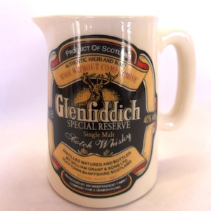 May include: White ceramic Glenfiddich Special Reserve Scotch Whisky mug with a black and gold label featuring a stag and the text "Product of Scotland, Authentic Highland Malt, Made Without Compromise, Glenfiddich Special Reserve, Single Malt Scotch Whisky, Distilled Matured and Bottled by William Grant & Sons Ltd, Dufftown Banffshire Scotland, 40% vol."