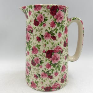 Peut inclure: Un pichet en céramique blanche avec un motif floral de roses roses et rouges. Le pichet a une anse et une large ouverture.