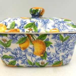 May include: A white ceramic butter dish with a lid. The dish is decorated with a lemon and floral pattern in shades of blue, green, and yellow.