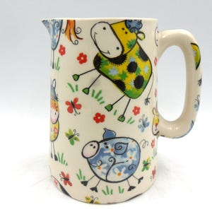 May include: A white ceramic jug with a handle features a whimsical design of colourful cartoon animals, including cows, pigs, and butterflies.