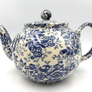 May include: A white teapot with a blue floral pattern. The teapot has a round body and a spout on the left side. The handle is on the right side.