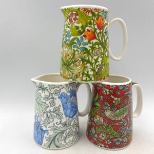 May include: Three ceramic jugs with floral patterns. The top jug has a green, yellow and red floral pattern. The middle jug has a blue and green floral pattern. The bottom jug has a red and green floral pattern.