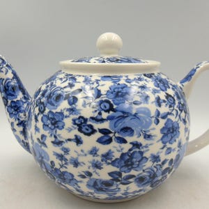 May include: A white teapot with a blue floral pattern. The teapot has a round body and a lid with a knob on top. The spout and handle are also white.